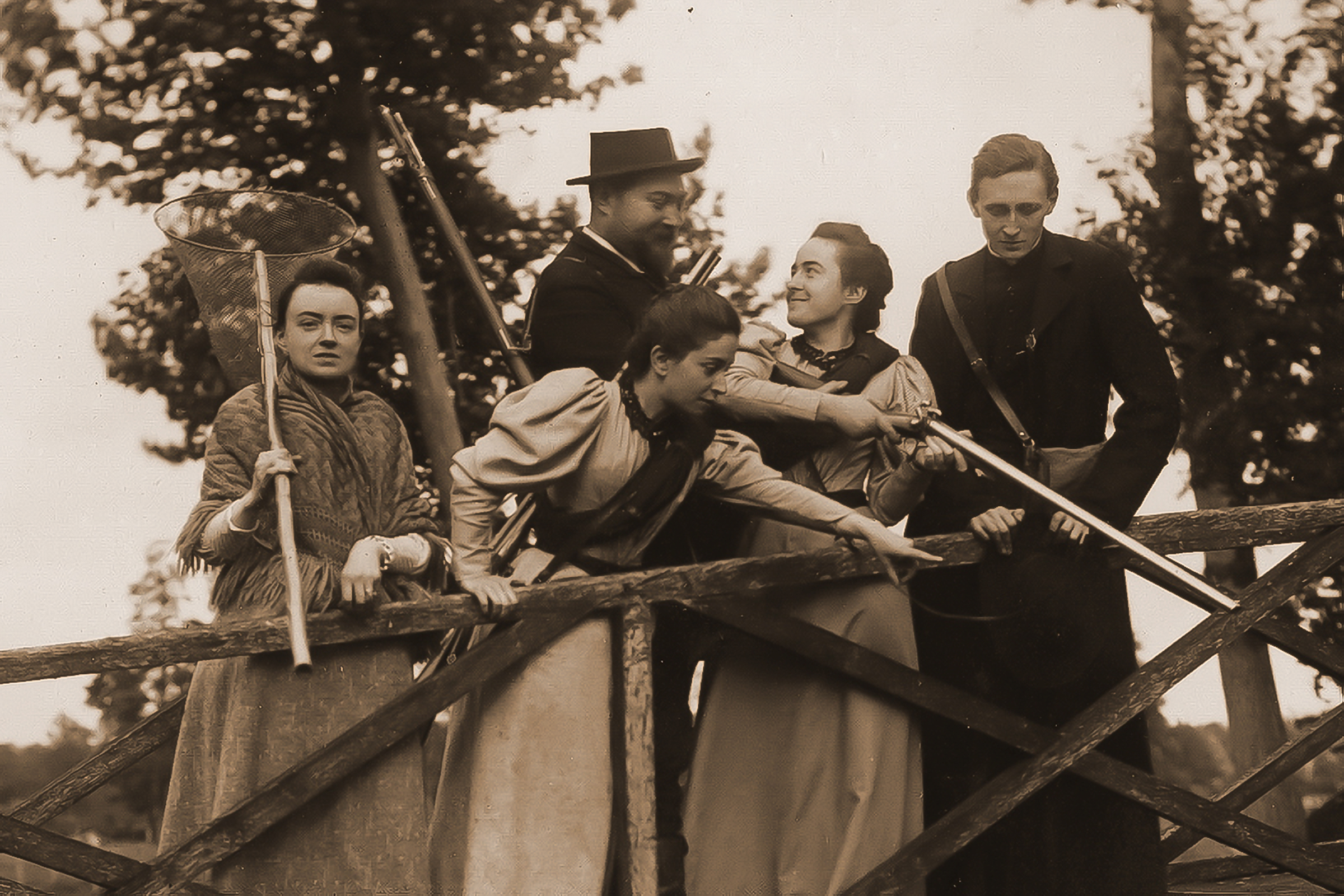 Céline Martin and companions pose with rifles and expedition props on a wooden bridge.