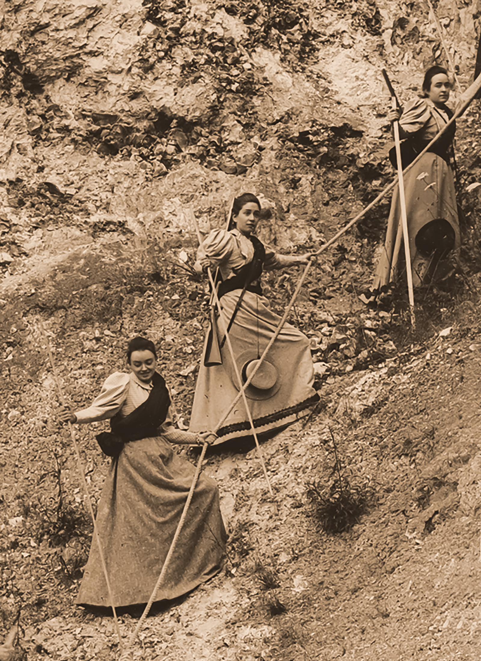 Three women in costume stage a roped descent down a steep hillside.