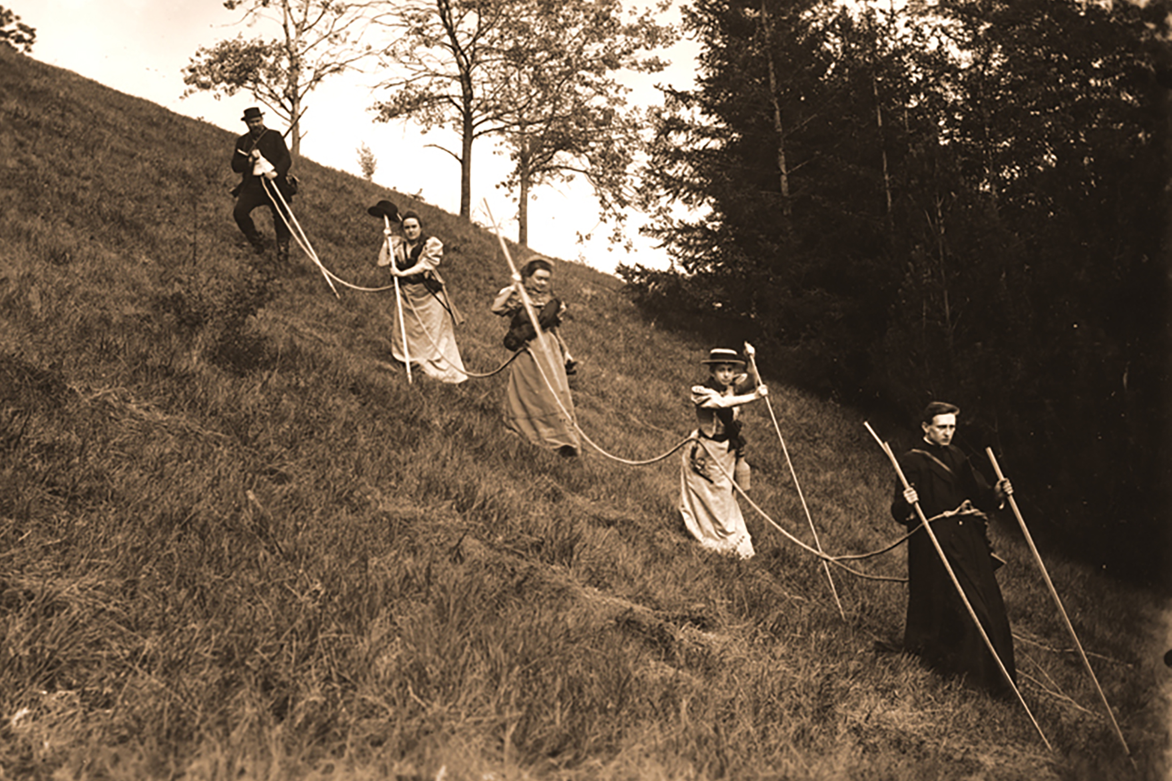 The costumed expedition party descends a hillside linked together by rope.